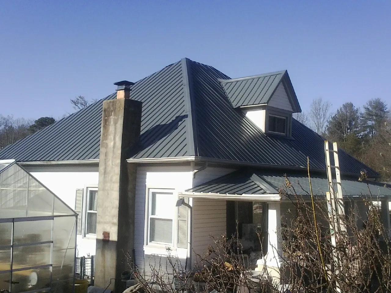 Dark blue standing seam metal roof on a white farmhouse with dormer — Slate & Tile Roof Repair by Roofing Brothers in Woodward