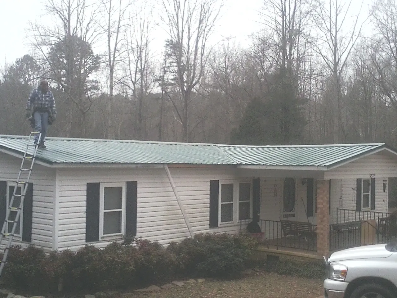 Worker on a ladder beside a new green metal roof on a ranch home in Woodward
