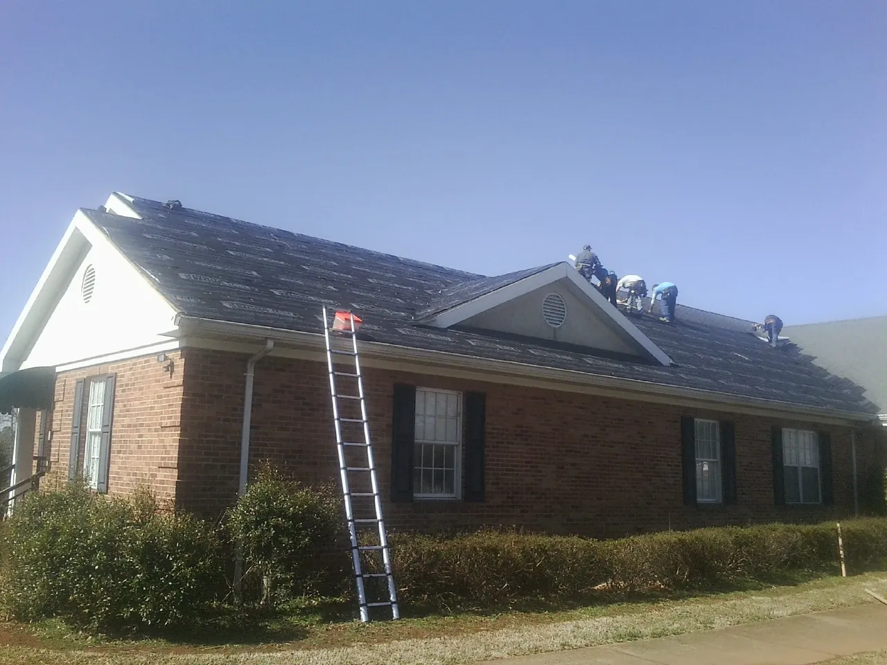 Crew tearing shingles off a brick ranch roof with a ladder set — Emergency Roof Repair work by our crew in Woodward