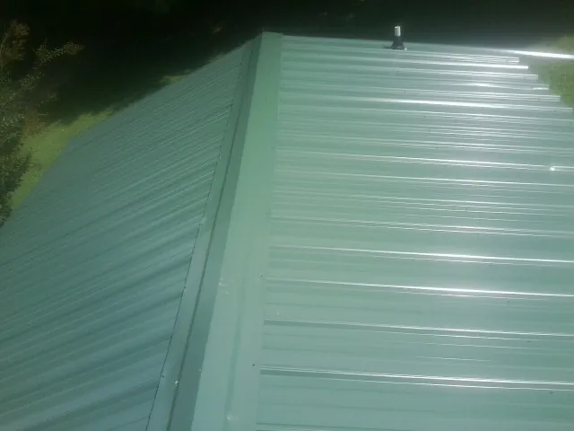 New green metal panels meeting at the ridge of a roof — Flat Roof Repair work by our crew in Woodward