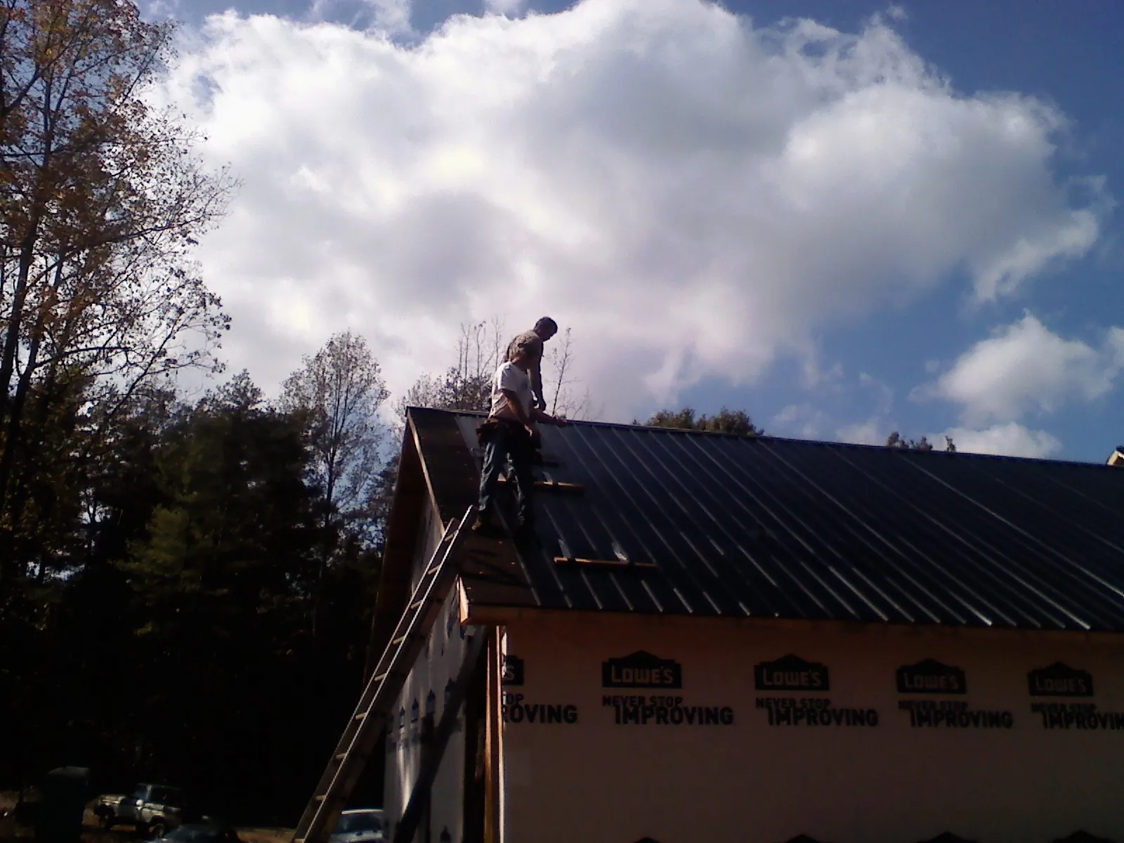 Roofer fastening dark metal panels high against a cloudy sky, from a Roof Inspection job in Woodward